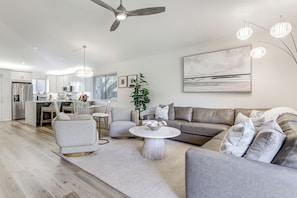 Een moderne woonkamer met een grijze bank, een ronde salontafel, en een eethoek met een witte tafel en stoelen.