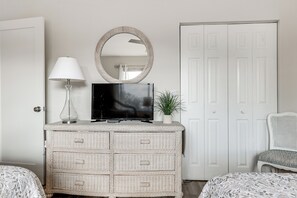 A bedroom with a TV, a lamp, a mirror, a dresser, a chair, and a wardrobe.