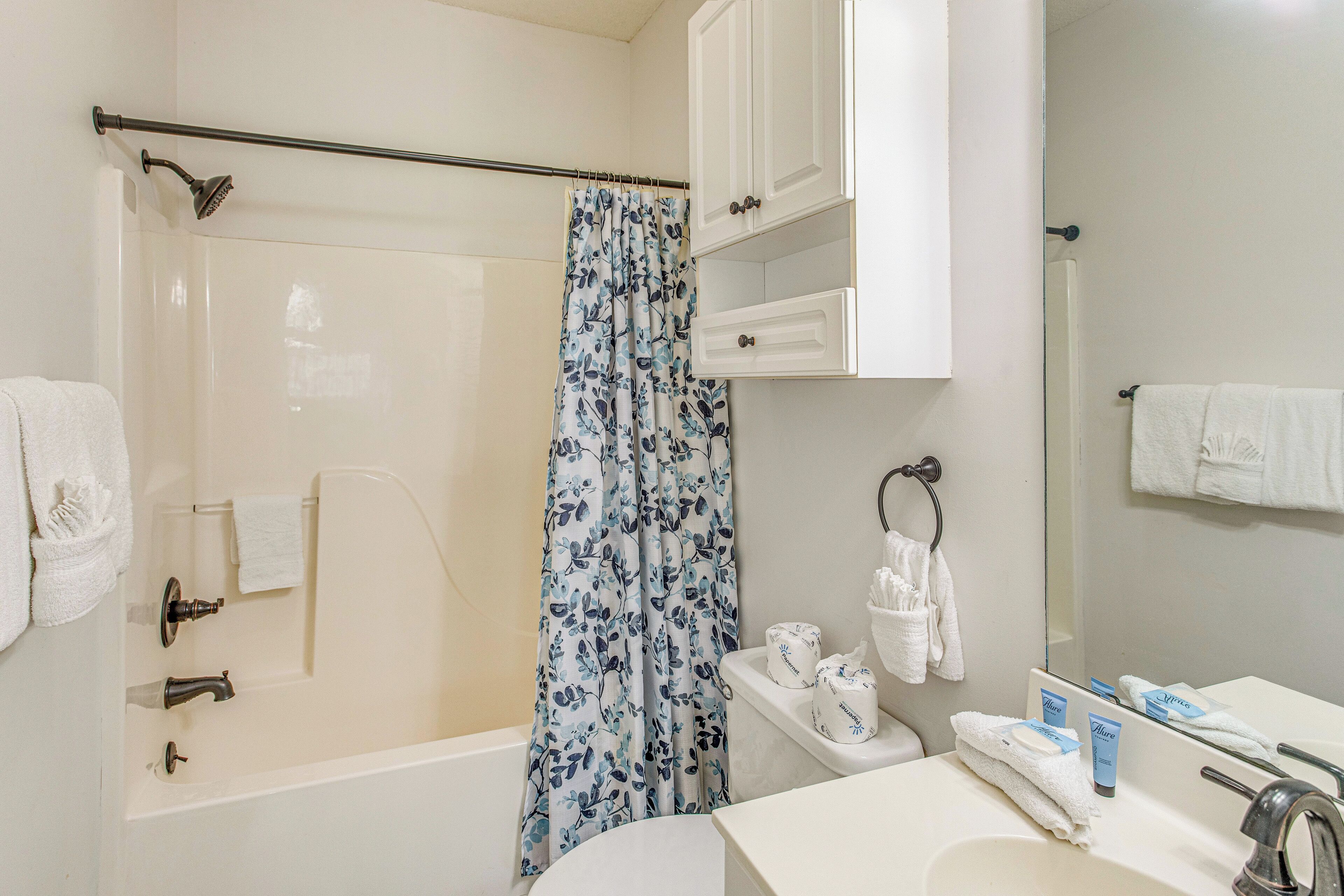 A bathroom with a bathtub, shower, and a toilet. There are towels and toiletries on the counter.
