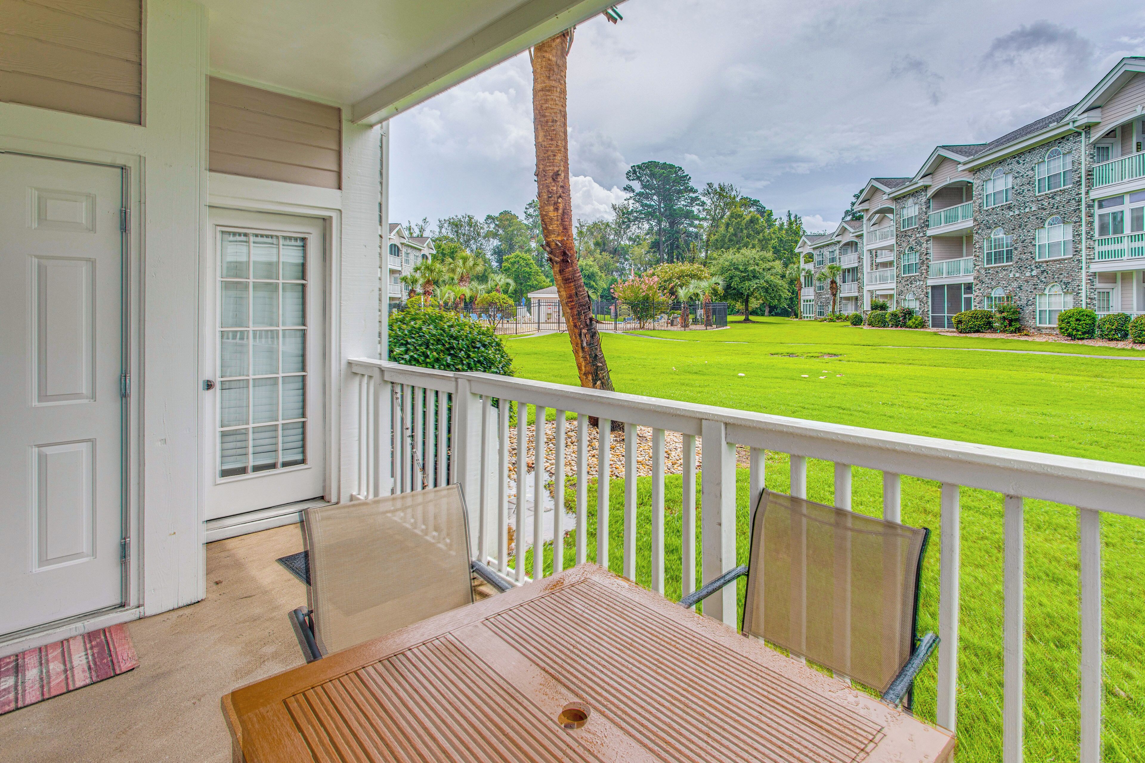 A porch with a table and chairs, overlooking a well-maintained lawn and a row of townhouses.