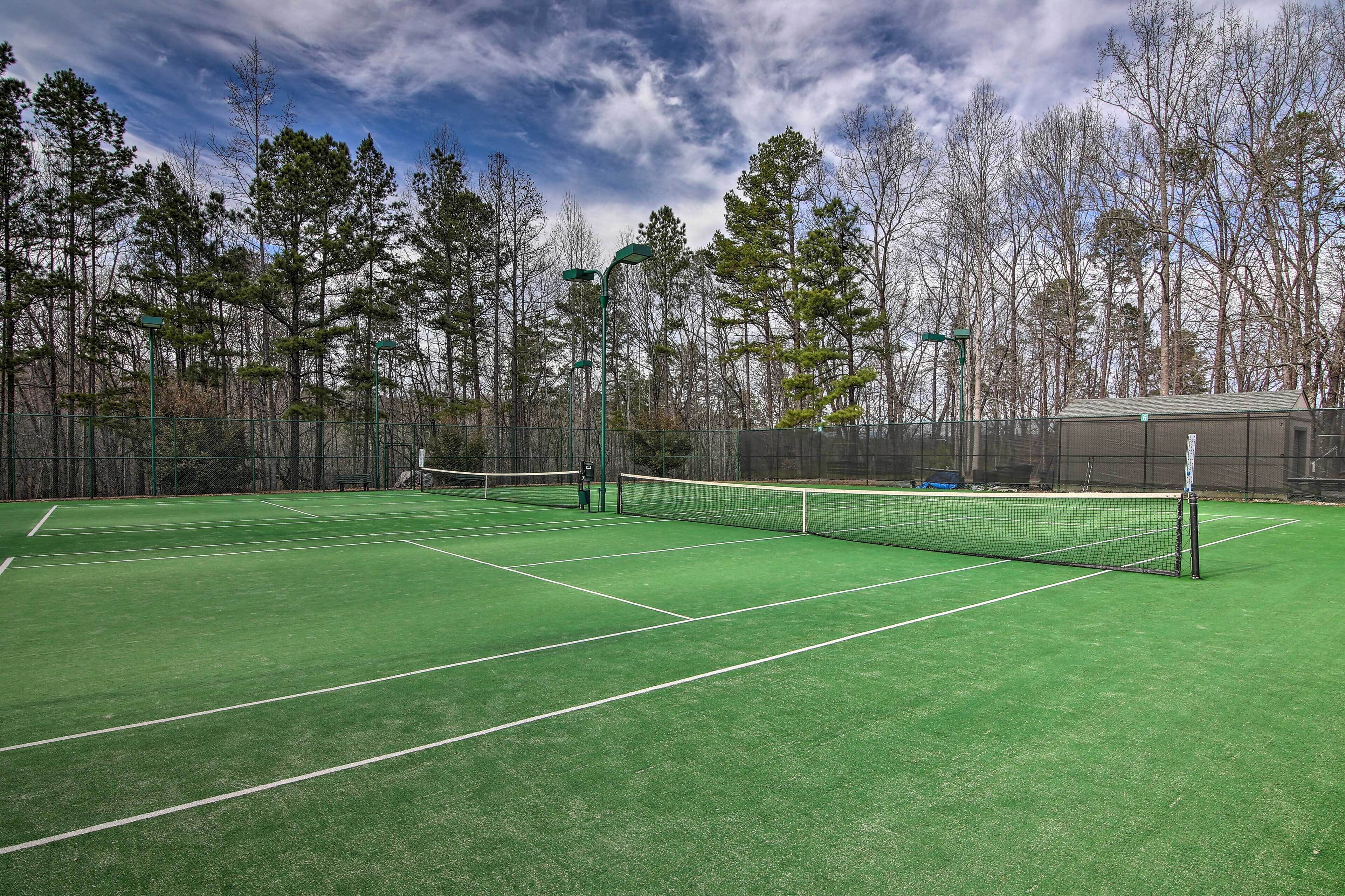 A tennis court with a net, surrounded by trees and a fence.