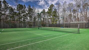 A tennis court with a net, surrounded by trees and a fence.