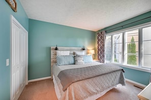 Um quarto com cama, janela com cortinas, mesa de cabeceira e luminária na parede.