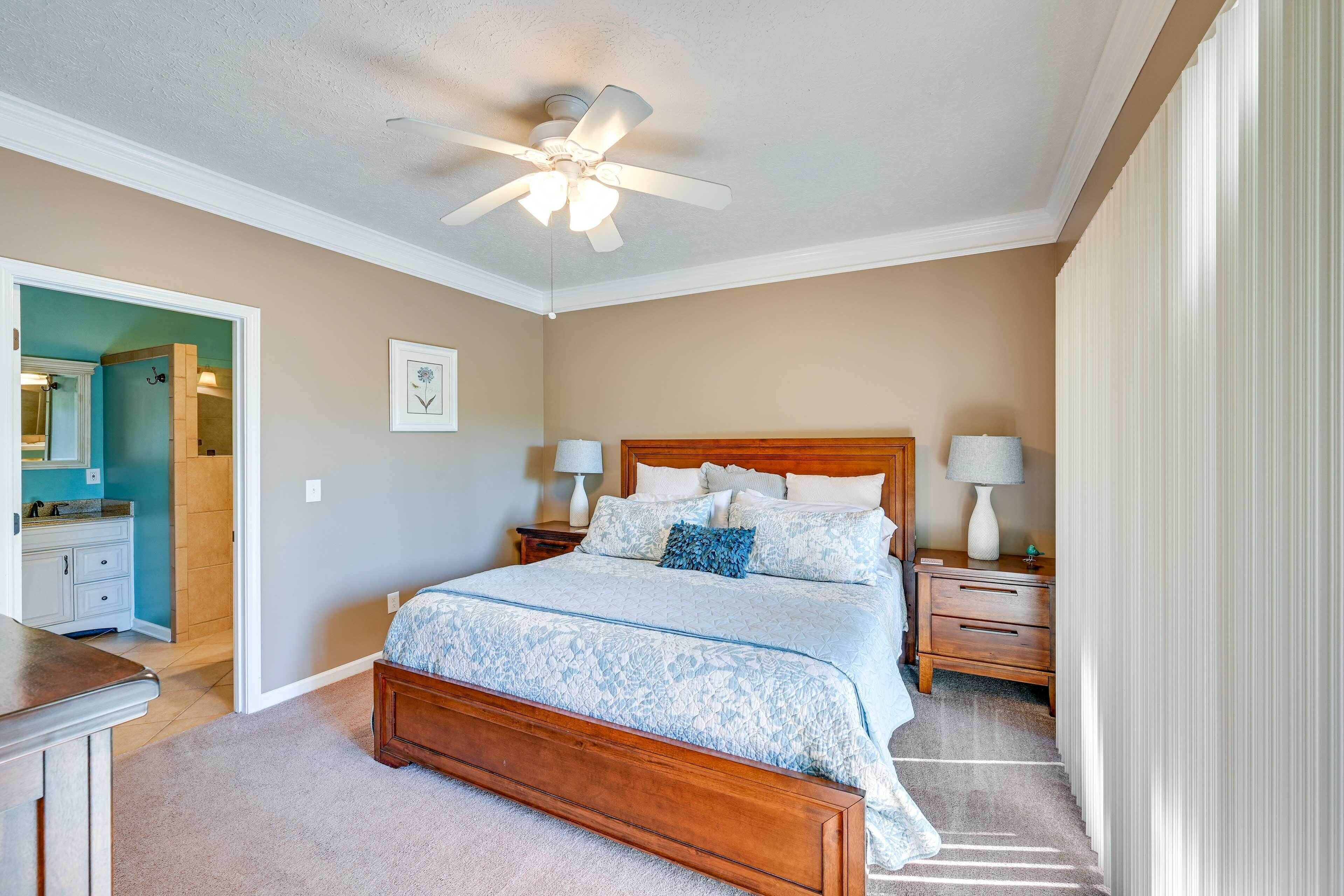 A bedroom with a wooden bed, two bedside tables with lamps, a ceiling fan, and a door leading to another room.