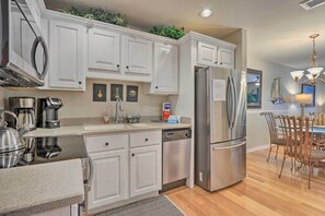 A modern kitchen with white cabinets, stainless steel appliances, and a dining area with wooden chairs. - Walk to Folly Field Beach: Island Escape w/ Pool (Hilton Head Island)