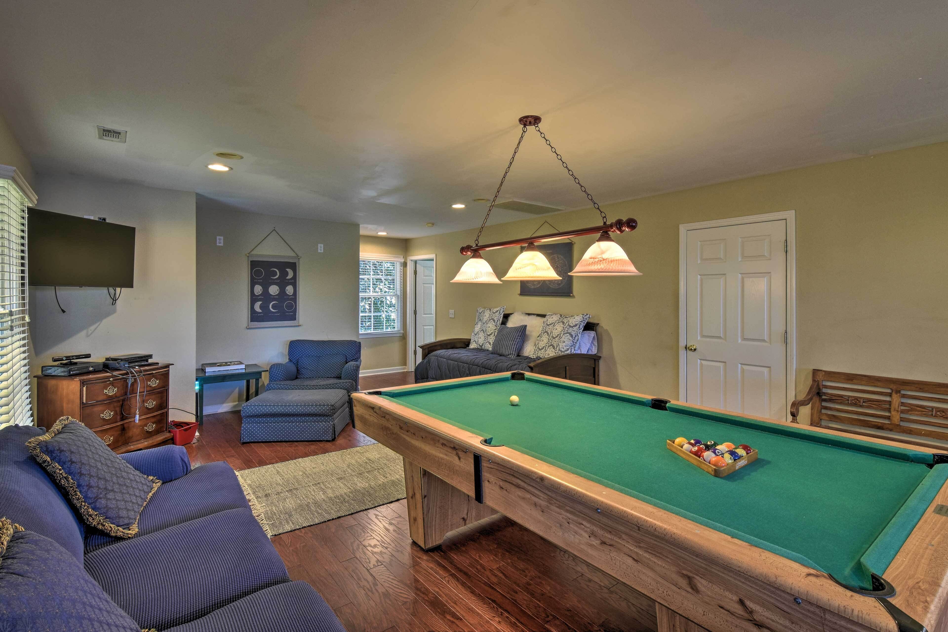 A pool table in a room with a sofa, a television, and a door.