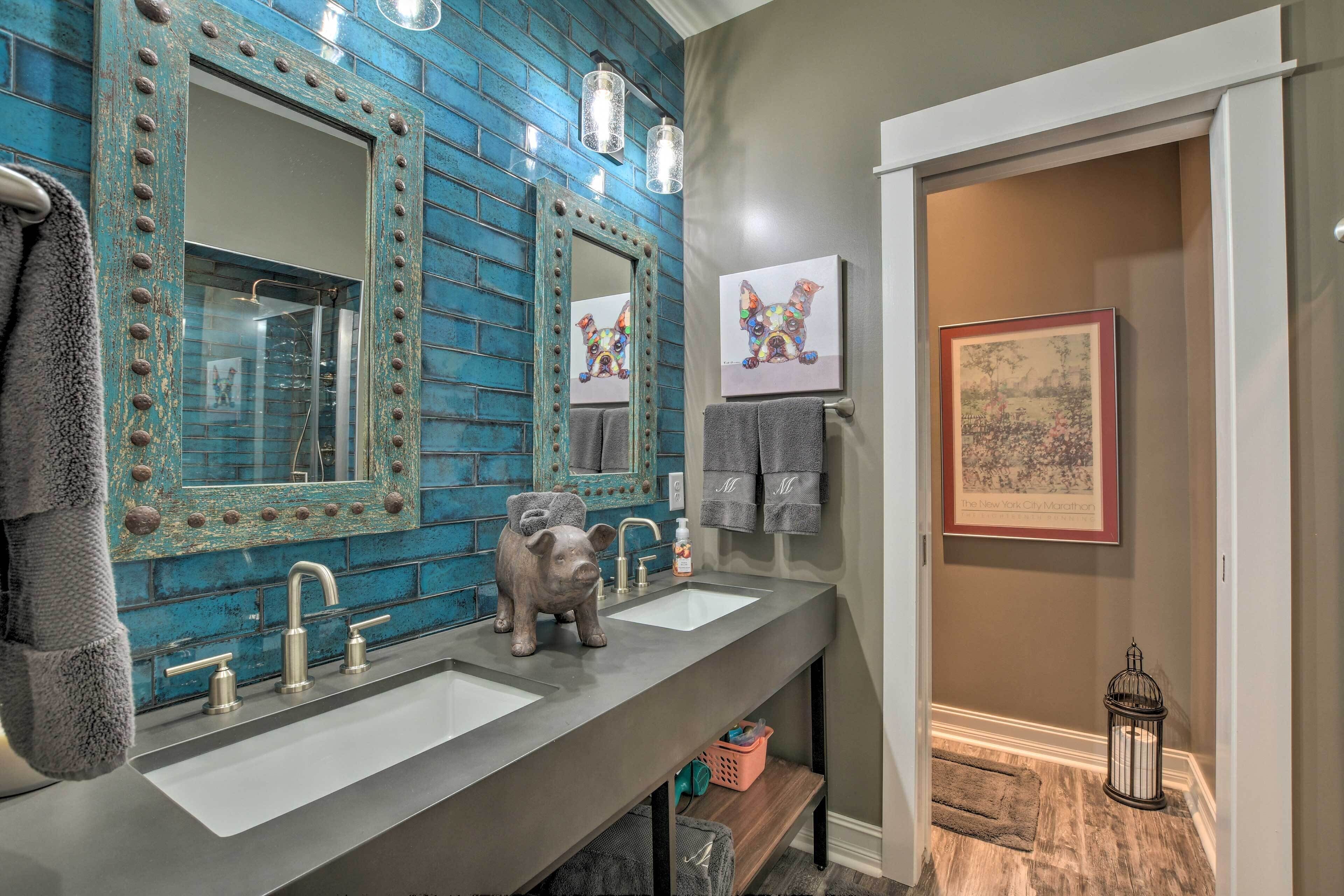 Une salle de bain avec un mur en briques bleues, deux lavabos, un distributeur de savon en forme de cochon et un tableau encadré accroché au mur.