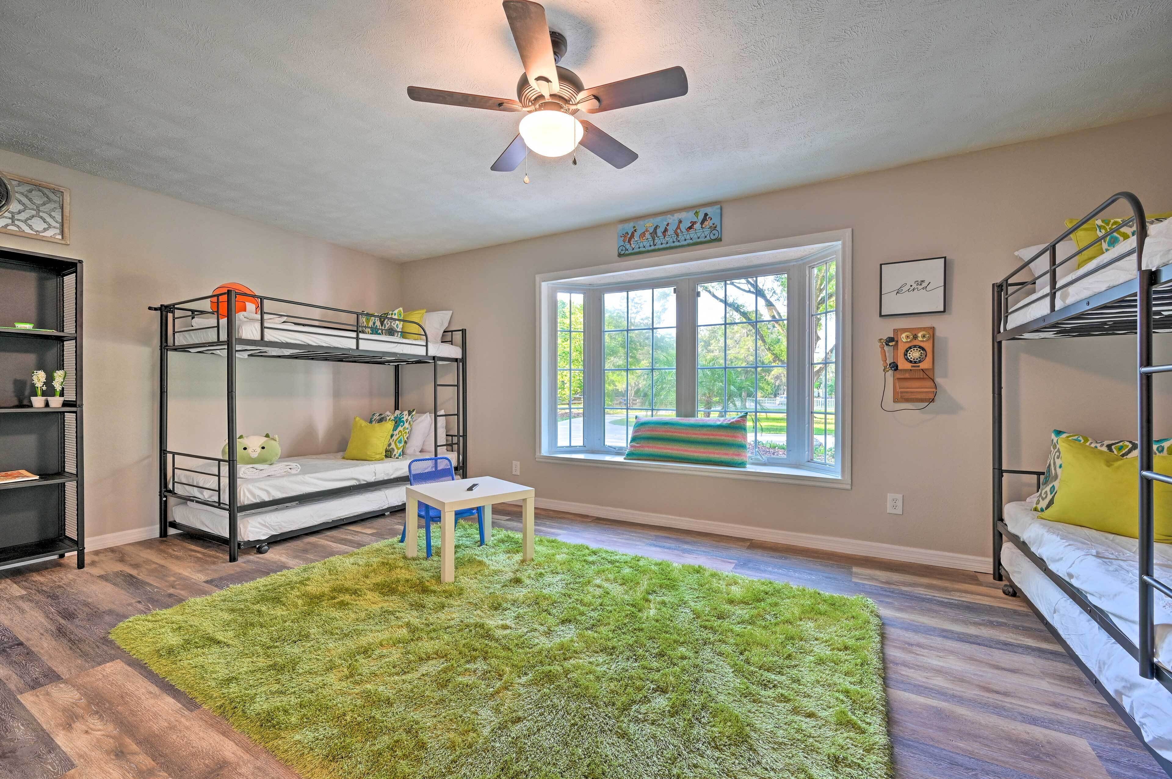 A child's room with bunk beds, a ceiling fan, a window with a view, and a bookshelf.