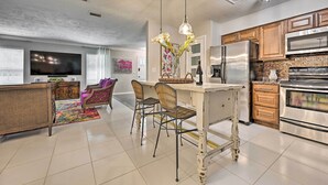 A modern kitchen with stainless steel appliances, a dining area with wicker chairs, and a flat-screen TV in the living room. - Huge Lutz Family Retreat w/ Game Room & Pool! (Lutz)