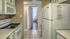 A kitchen with white appliances, including a stove, microwave, and refrigerator, with a tiled floor and a door leading to another room. - Walk to Family Kingdom: Retreat w/ Pool (Myrtle Beach)