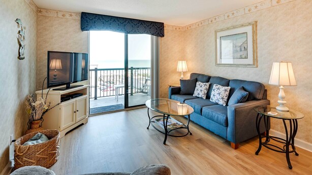 A living room with a sofa, two lamps, a glass coffee table, a television on a cabinet, and a wicker basket. - Walk to Family Kingdom: Retreat w/ Pool (Myrtle Beach)
