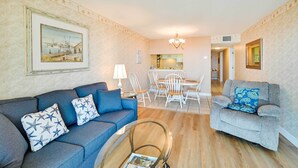 A living room with a blue sofa, a grey sofa, and a glass coffee table. There is a dining area with a white table and chairs. - Walk to Family Kingdom: Retreat w/ Pool (Myrtle Beach)