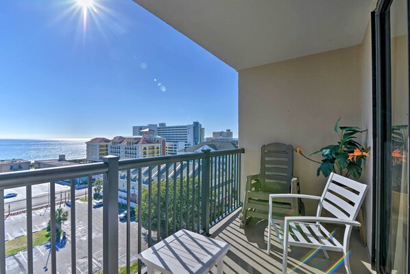 A balcony with a view of the ocean and cityscape, featuring a table and two chairs.