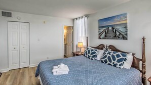 A bedroom with a bed, a painting of a beach, a white door, and a nightstand with a lamp. - Walk to Family Kingdom: Retreat w/ Pool (Myrtle Beach)