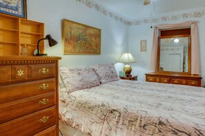 A bedroom with a bed, wooden dresser, lamp, and a painting on the wall.