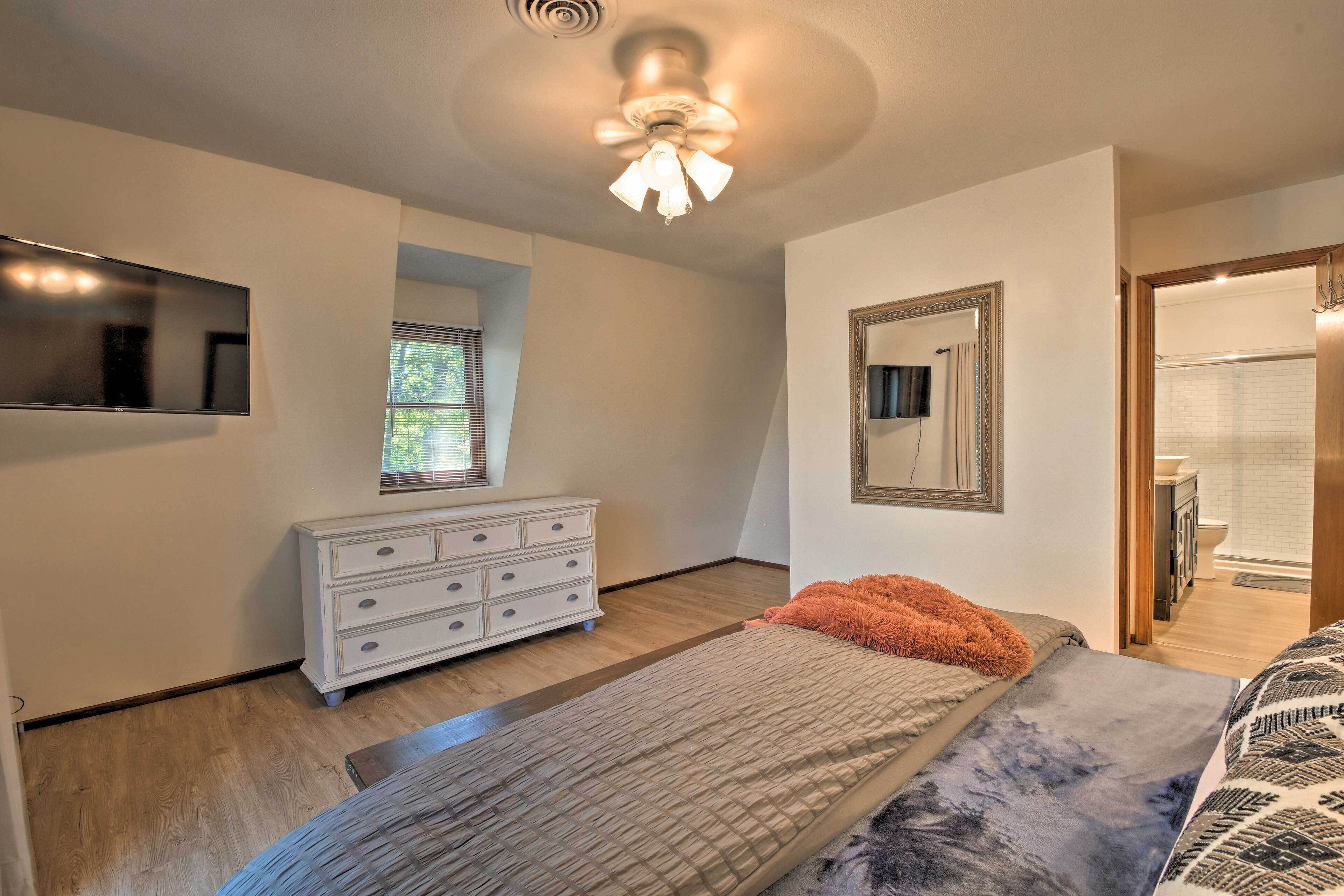 A bedroom with a bed, a dresser, a ceiling fan, a mirror, and a window.