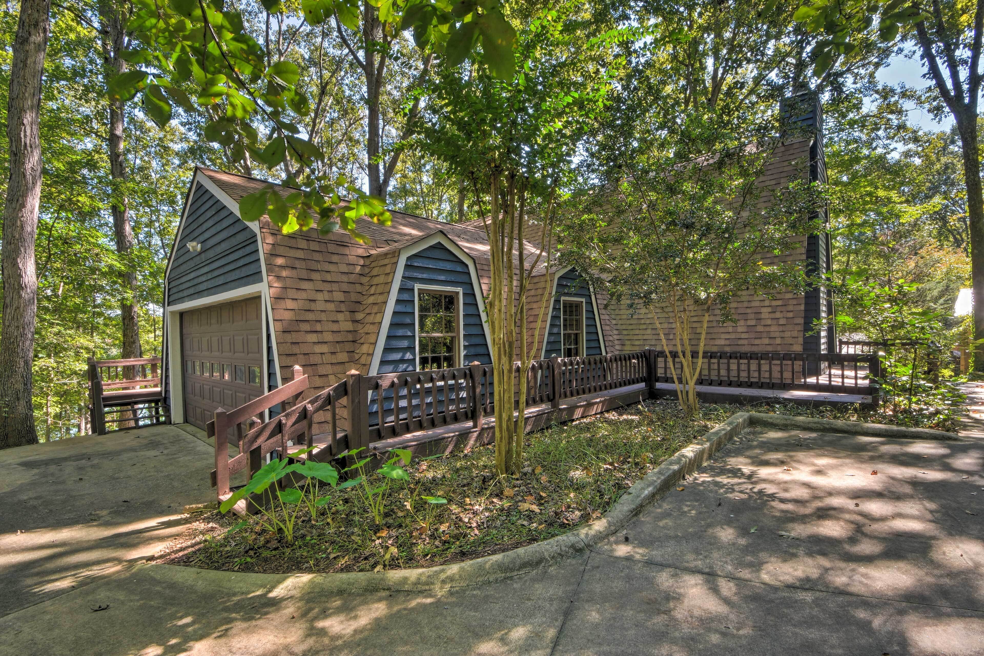A cabin with a garage, surrounded by trees and a wooden deck.