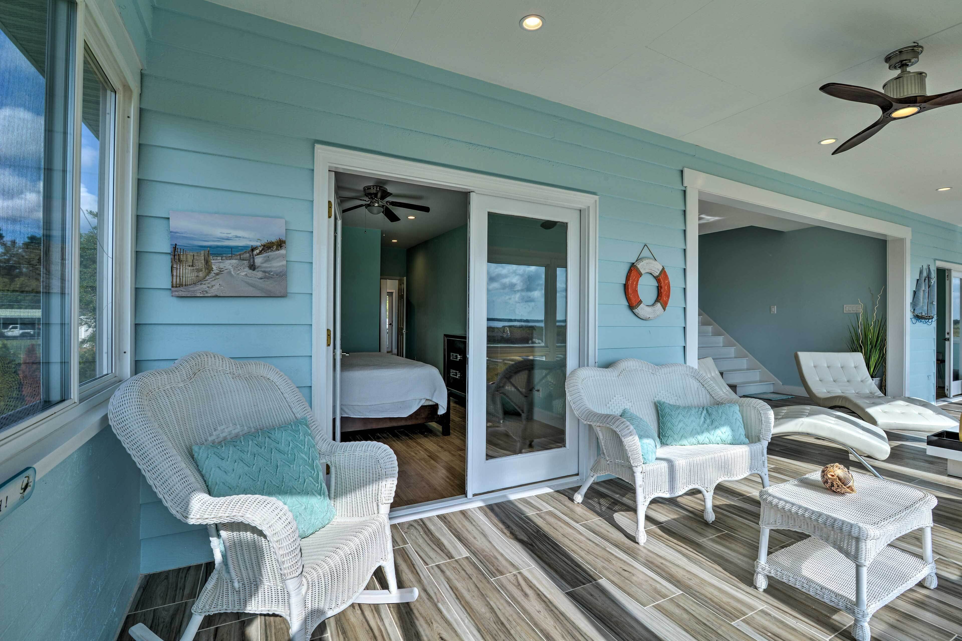 A room with a bed, white wicker chairs, a small table, and a ceiling fan.