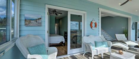 A room with a bed, white wicker chairs, a small table, and a ceiling fan.