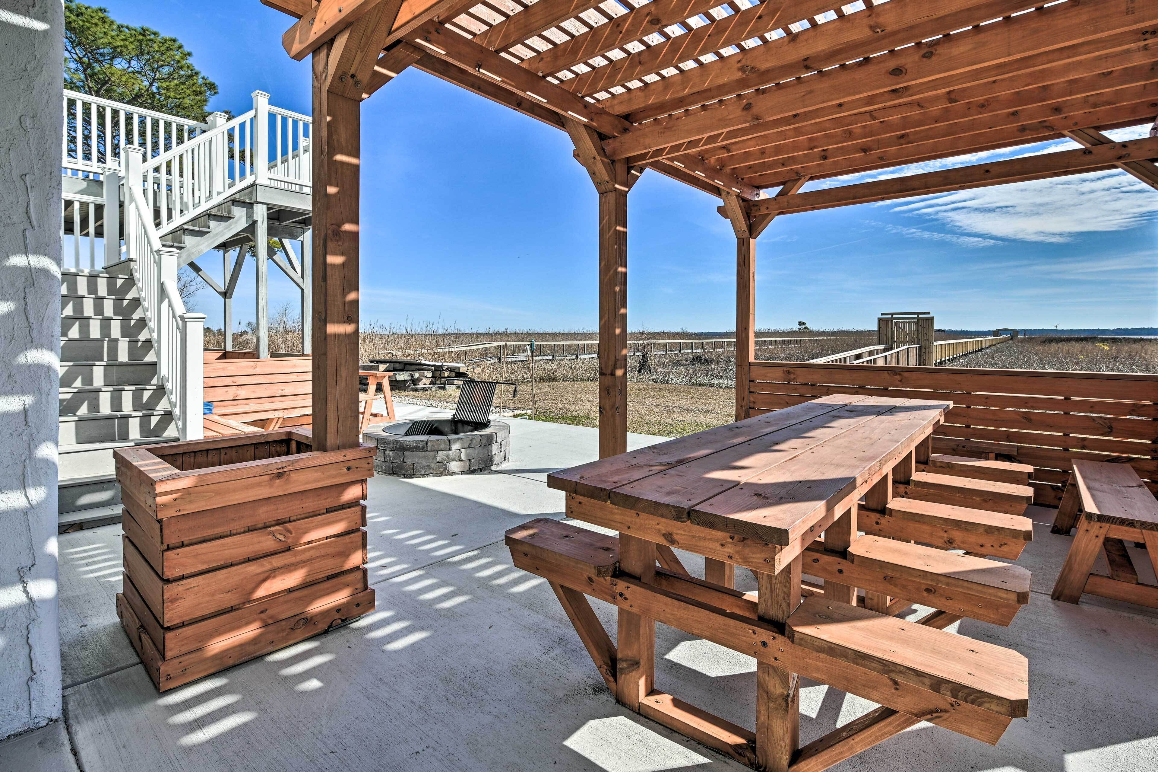 A wooden deck with picnic tables and a fire pit, overlooking a beach.