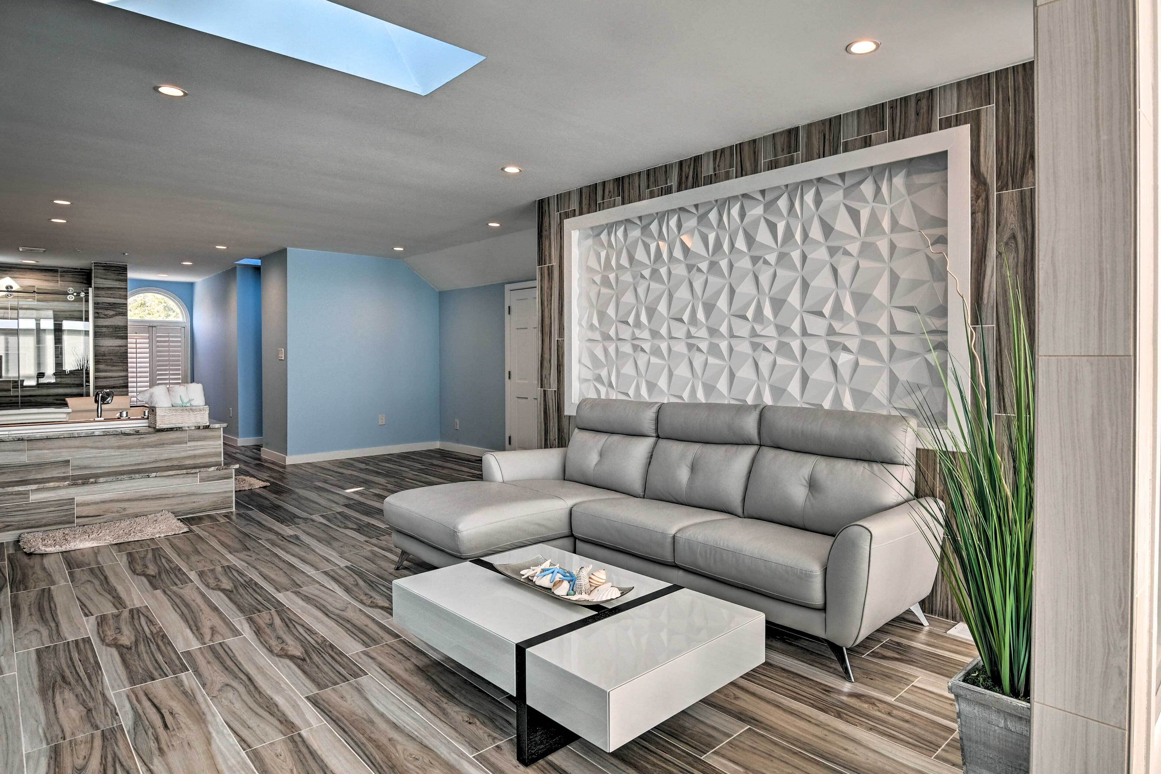 A modern living room with a grey sectional sofa, a glass coffee table, and a geometric wall panel.