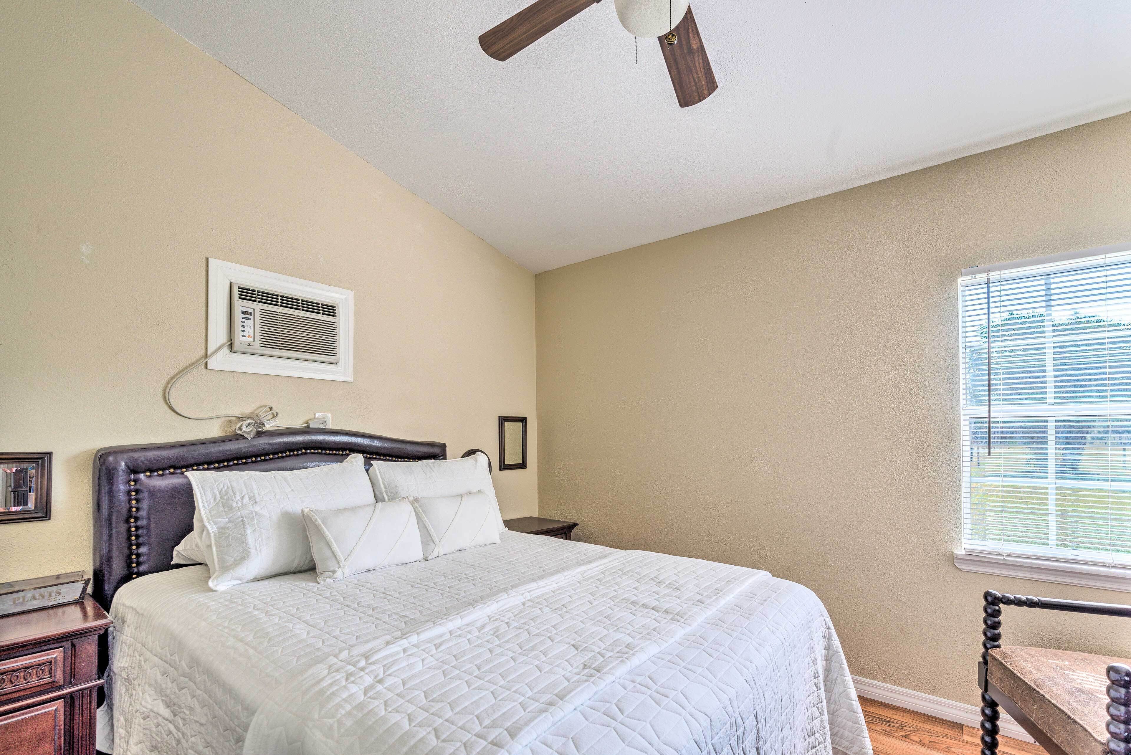 A bedroom with a bed, a ceiling fan, a window, and a wall-mounted air conditioner.