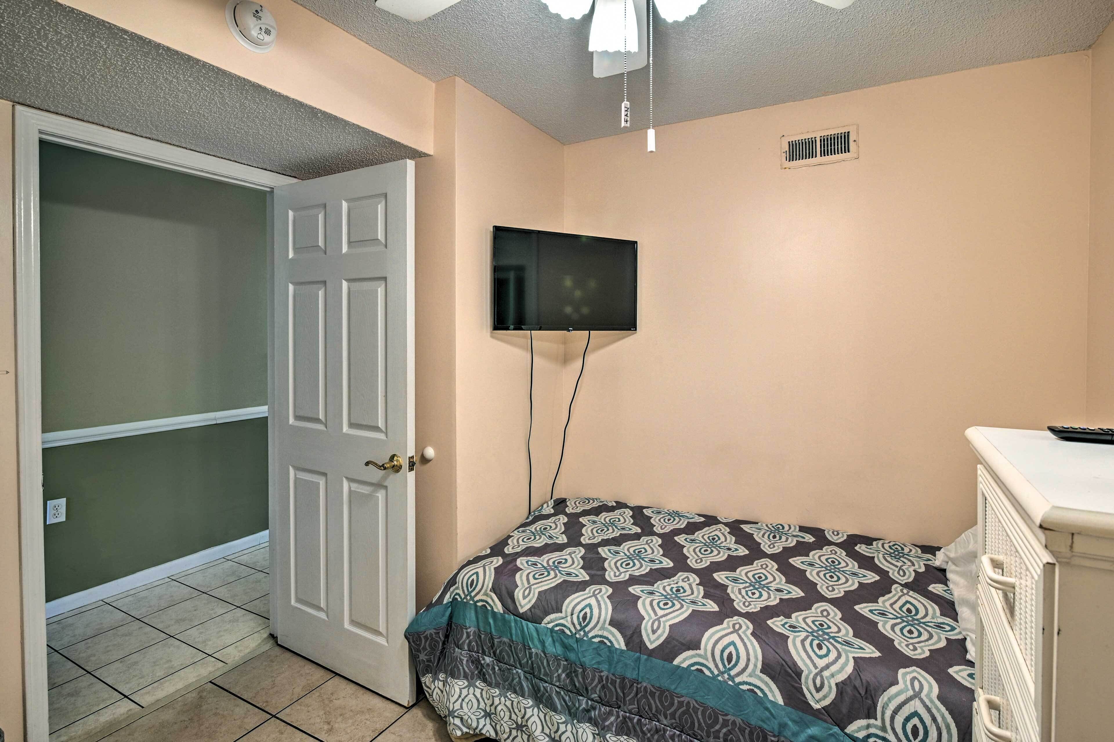 A bedroom with a bed, a television mounted on the wall, and a door leading to another room.