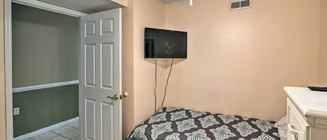 A bedroom with a bed, a television mounted on the wall, and a door leading to another room.