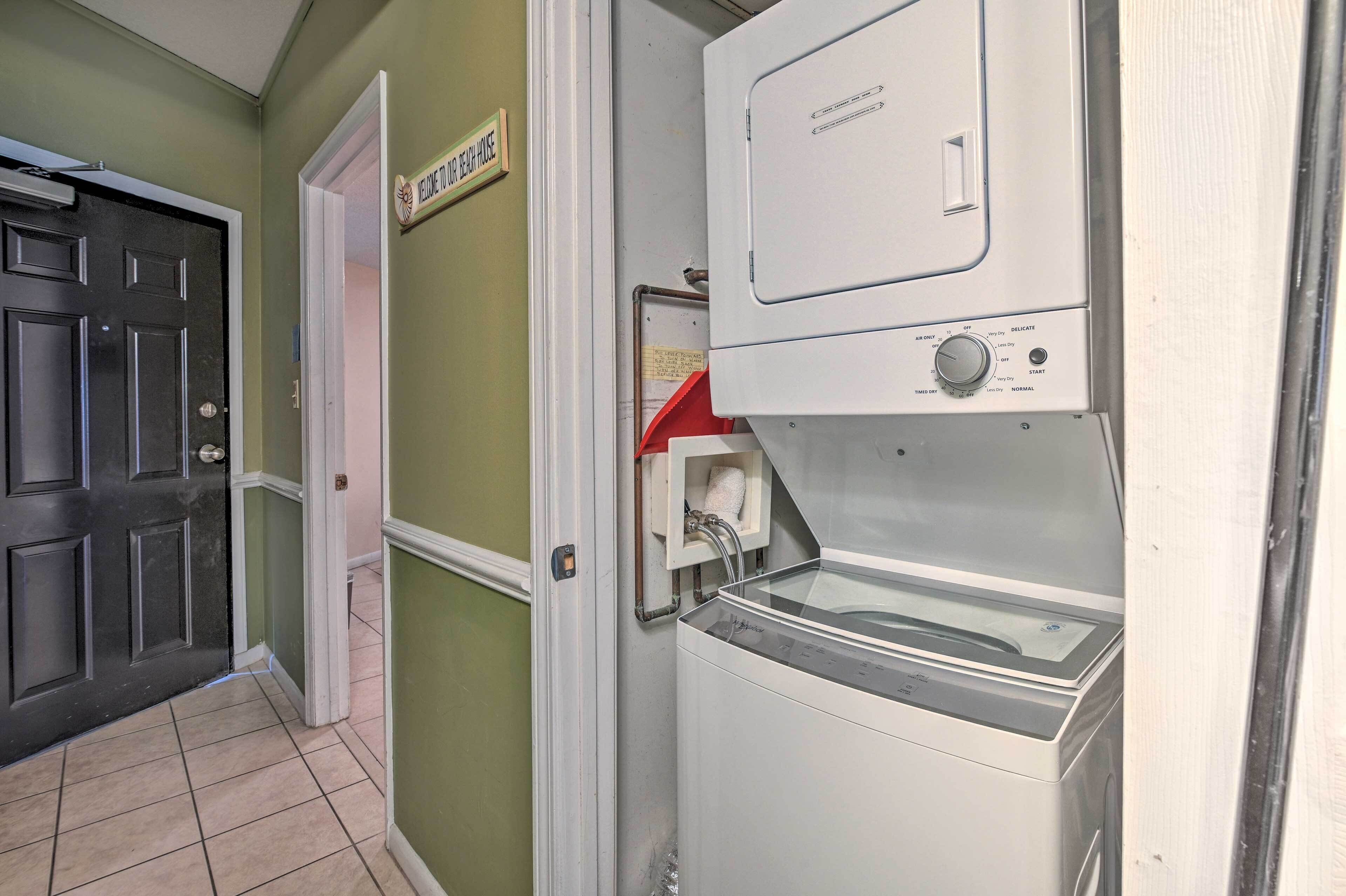 A laundry room with a front-loading washer and dryer, a door with a sign, and a tiled floor.