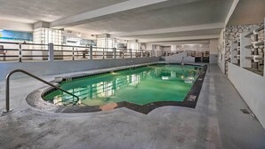 Una piscina interior con piso de concreto, un trampolín y una pared de piedra.