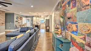 Ein modernes Wohnzimmer mit einem grauen Ecksofa, einem Essbereich mit blauem Tisch und einer Küche im Hintergrund.