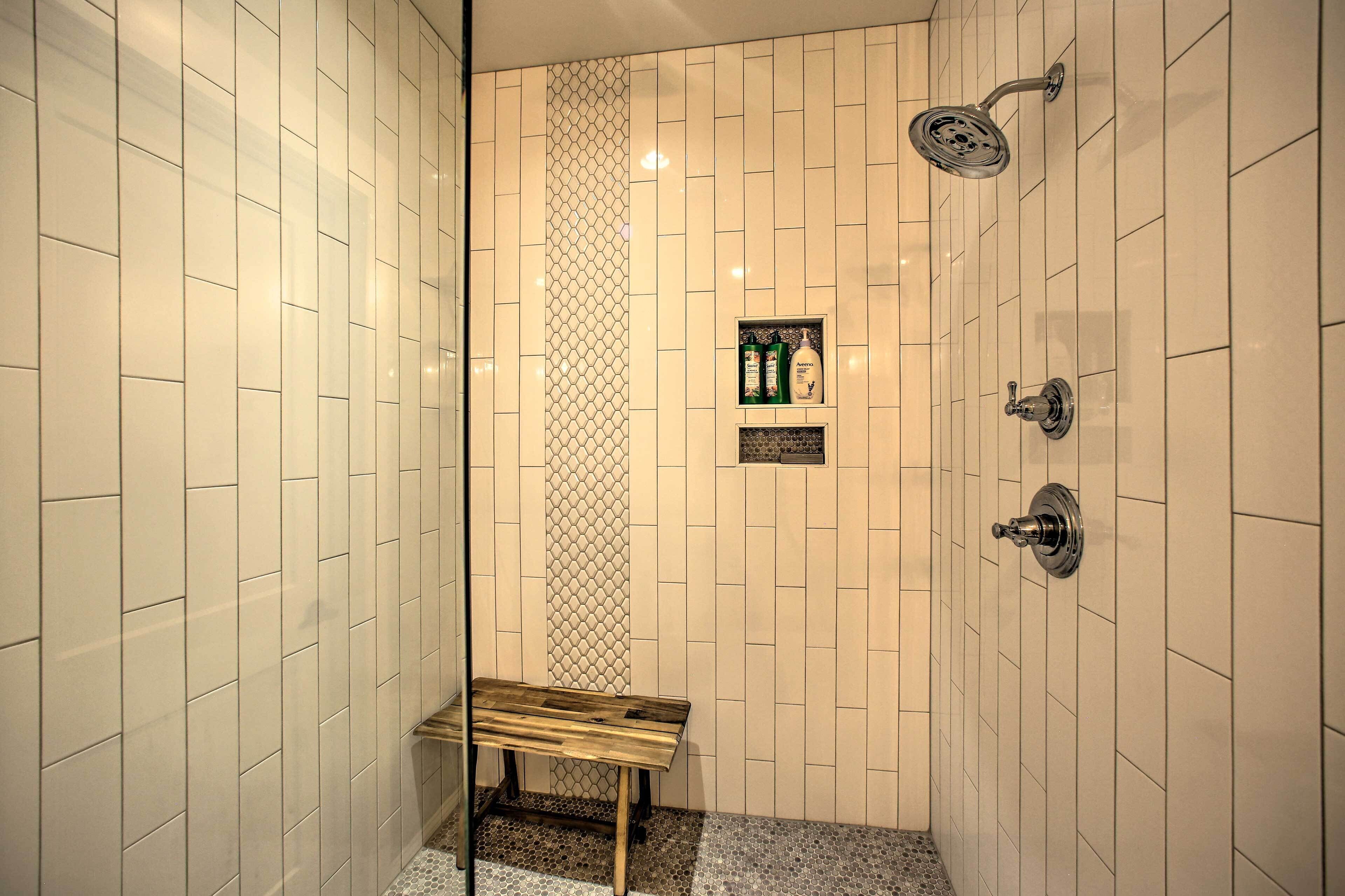 Un espace douche avec des murs recouverts de carreaux blancs, un banc et une pomme de douche.