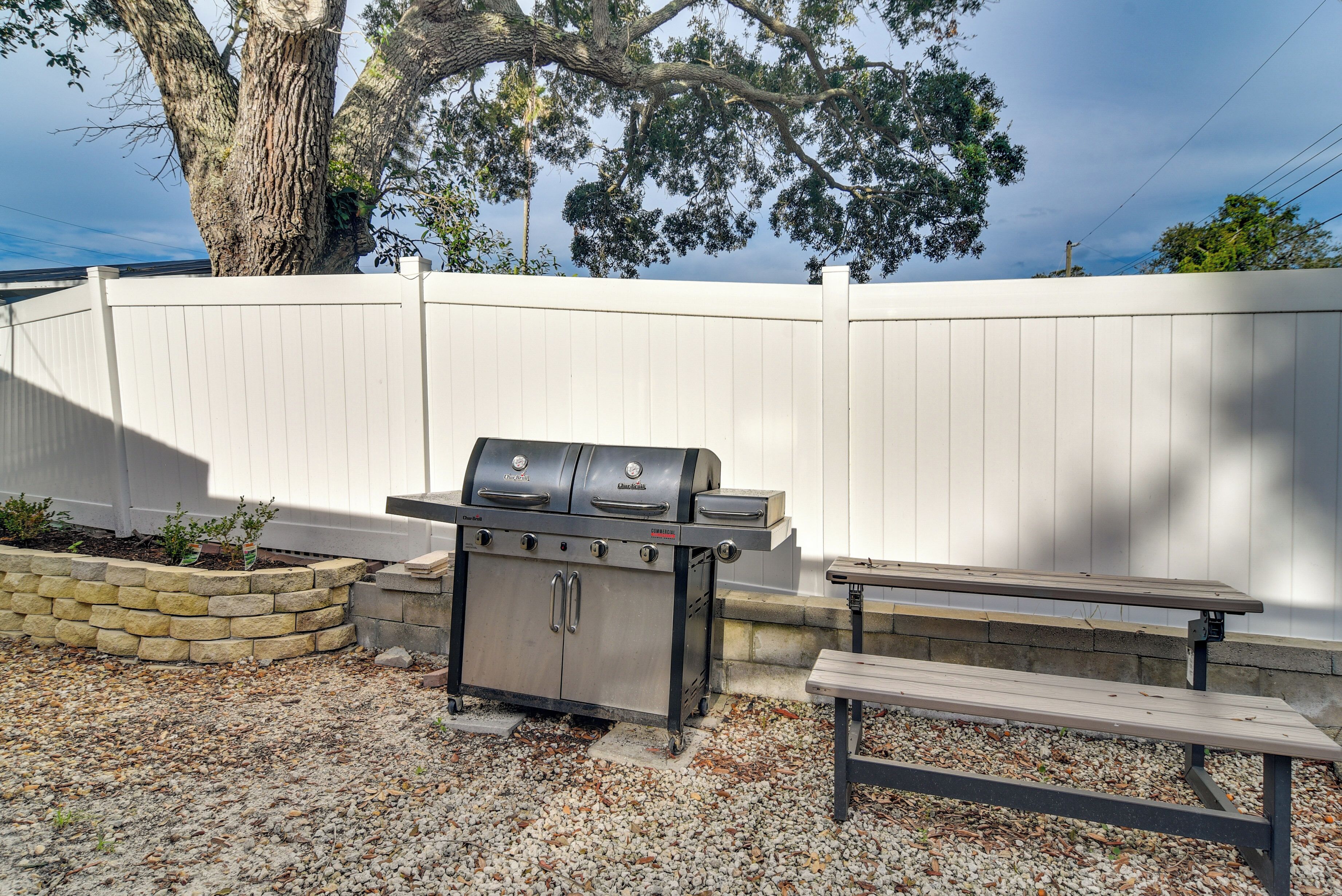 A barbecue grill with a stone wall and a bench in a backyard.