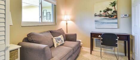 A living room with a beige wall, a brown sofa, a lamp, a desk, and a painting of a beach scene.