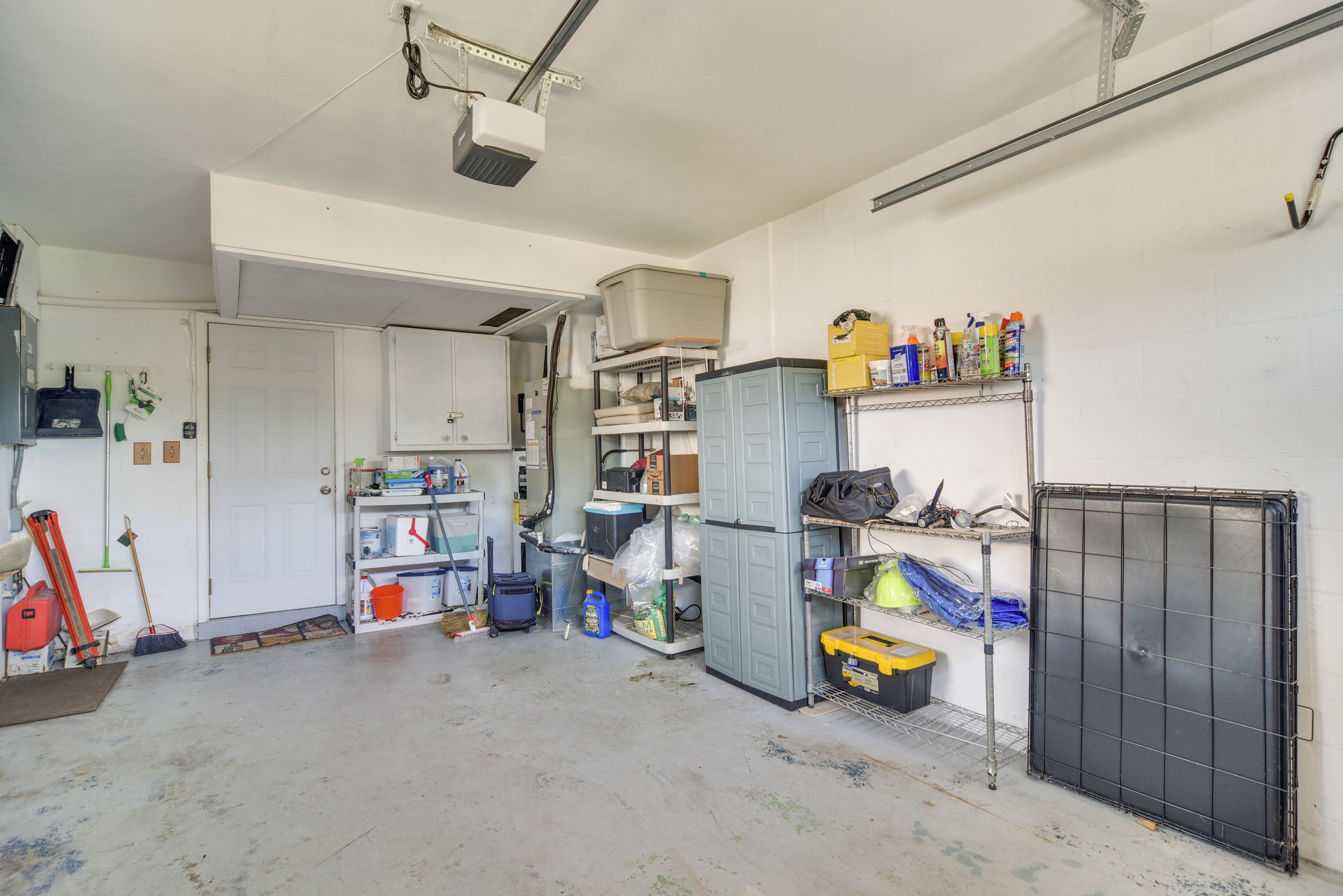 A cluttered room with a door, shelves with various items, and a large black metal gate.