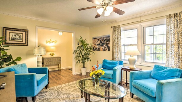 A living room with two blue sofas, a glass coffee table, a ceiling fan, and a large window with curtains. - Lovely Taylors Home: 8 Mi to Dtwn Greenville! (Taylors)