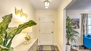 A well-lit hallway with a white door, a welcome sign, a potted plant, a lamp, and a blue armchair in a living area. - Lovely Taylors Home: 8 Mi to Dtwn Greenville! (Taylors)