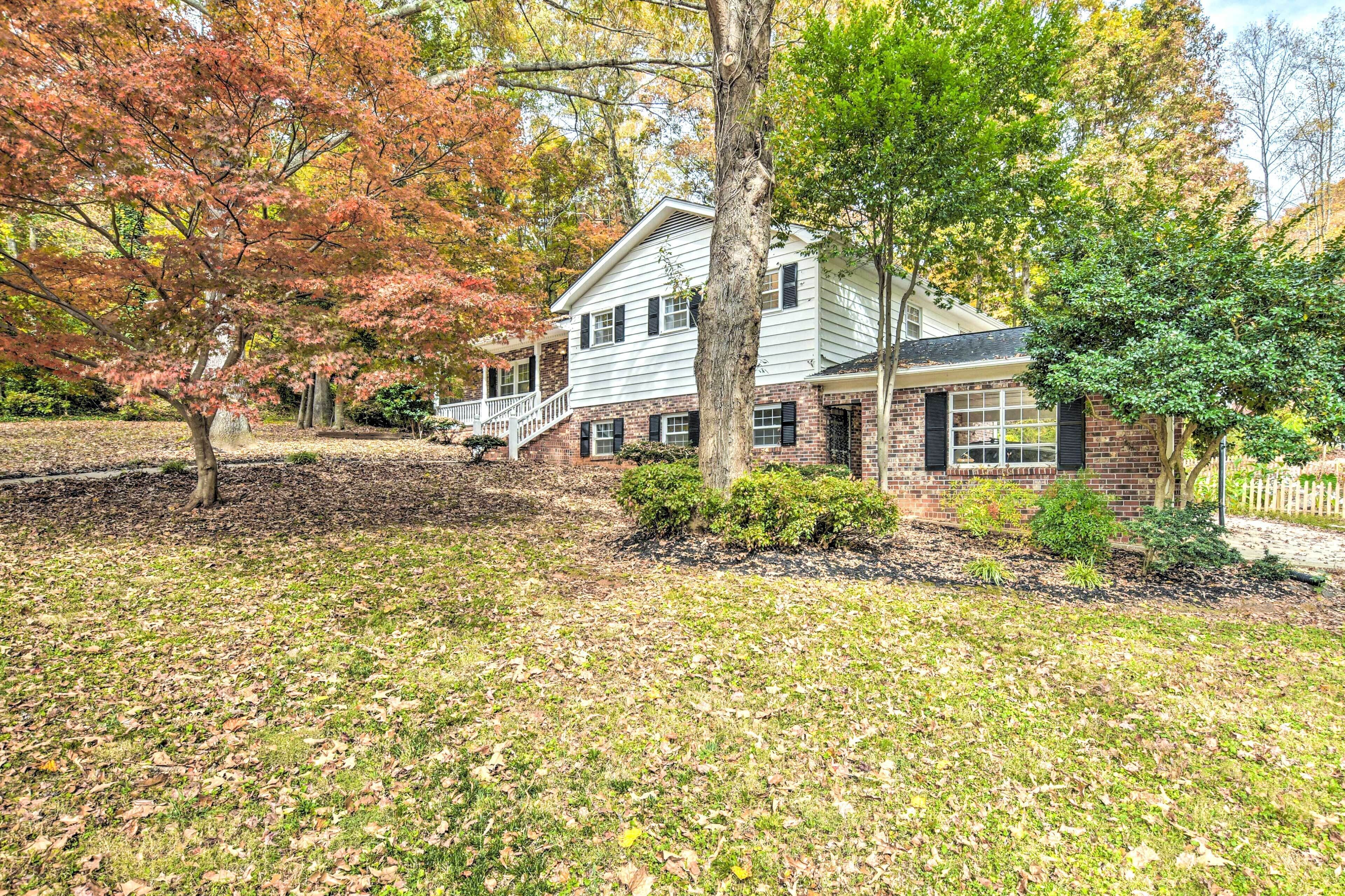 A two-story house with a brick facade and white siding, surrounded by a well-maintained lawn and trees with autumn foliage.