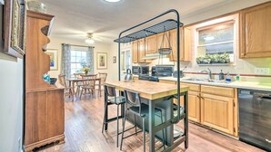 A kitchen with wooden cabinets, a central island with bar stools, a hanging rack, and a dishwasher. - Lovely Taylors Home: 8 Mi to Dtwn Greenville! (Taylors)