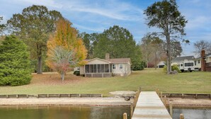 A house with a dock extending into a pond, surrounded by trees and a grassy area. - Lakefront House w/ Boat Ramp, Dock & Sunset Views! (Cross Hill)