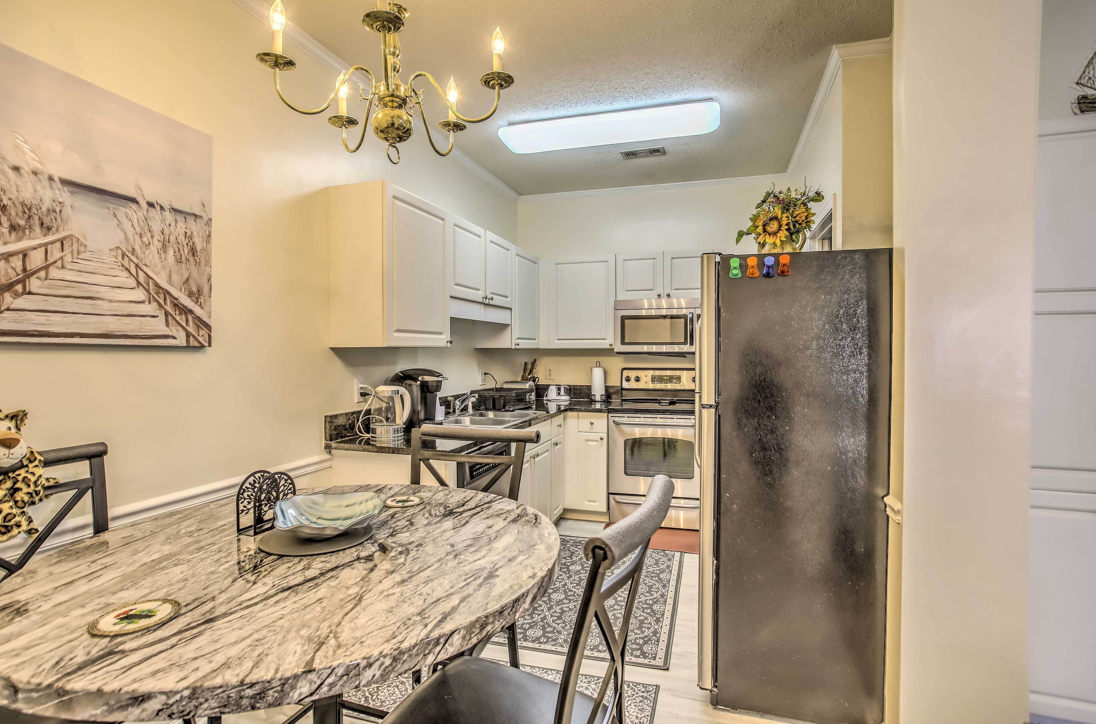 A kitchen with white cabinets, a marble dining table, a chandelier, and a refrigerator with magnets.