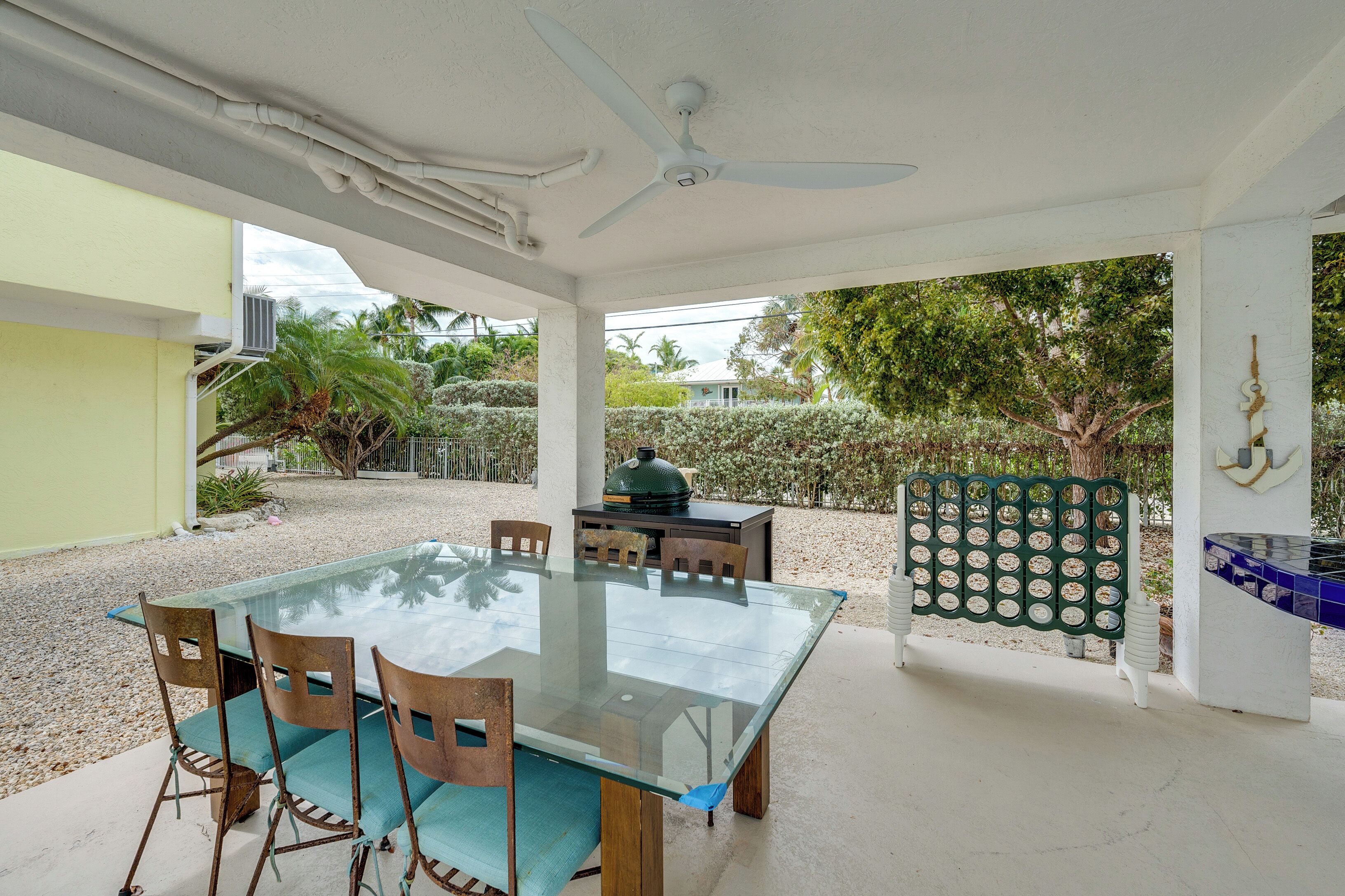 An outdoor patio with a glass-top table and chairs, a ceiling fan, and a grill.