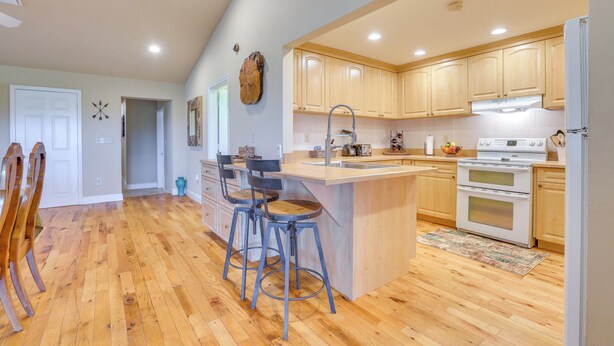 A kitchen with wooden cabinets, a central island with stools, a double oven, and a sink.