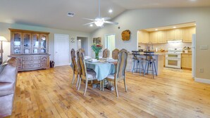 A spacious dining area with a wooden floor, a dining table with chairs, and a ceiling fan.