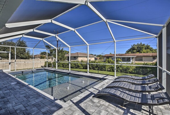 A covered outdoor swimming pool with lounge chairs and a brick patio.