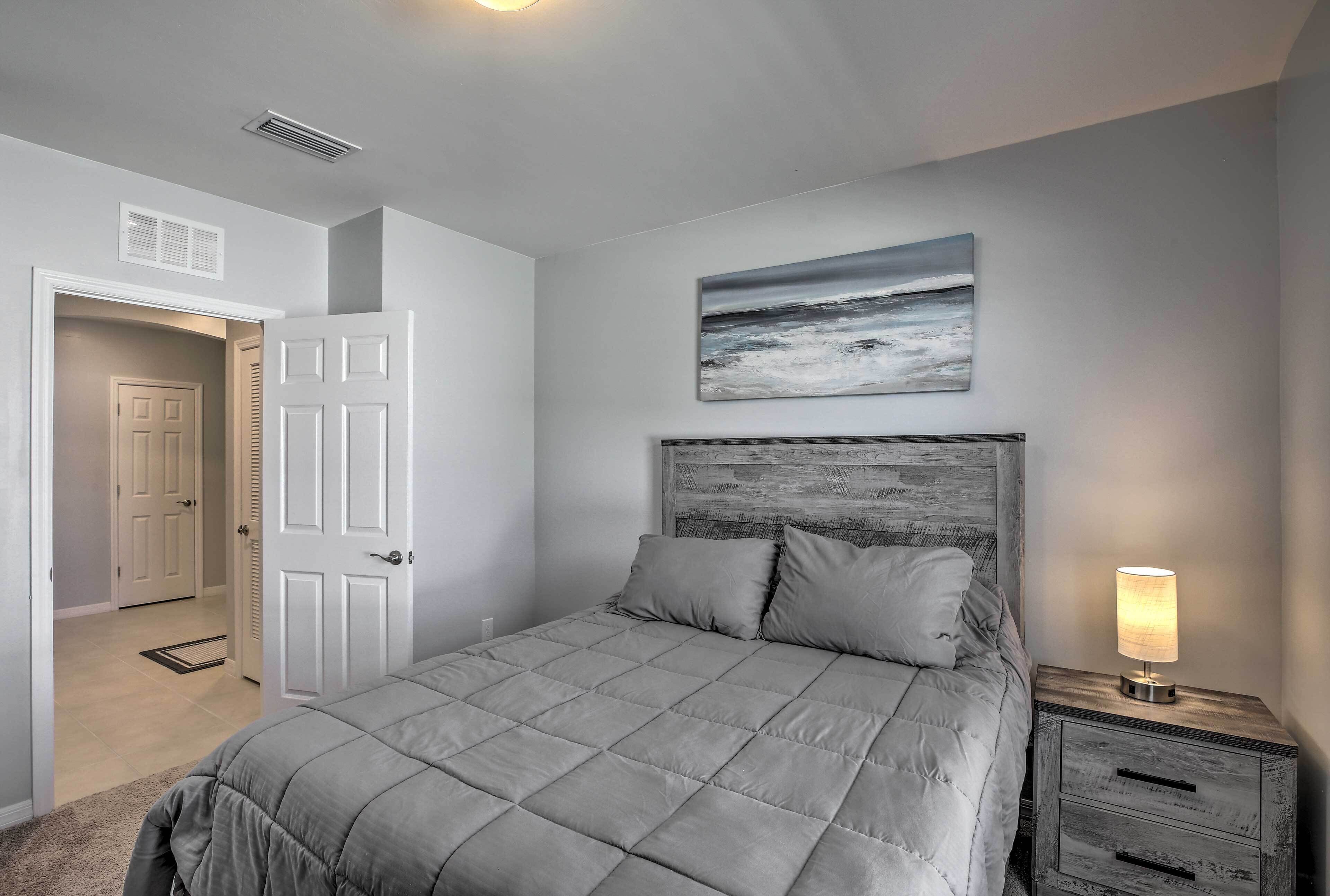 A bedroom with a bed, a nightstand with a lamp, a door, and a painting on the wall.