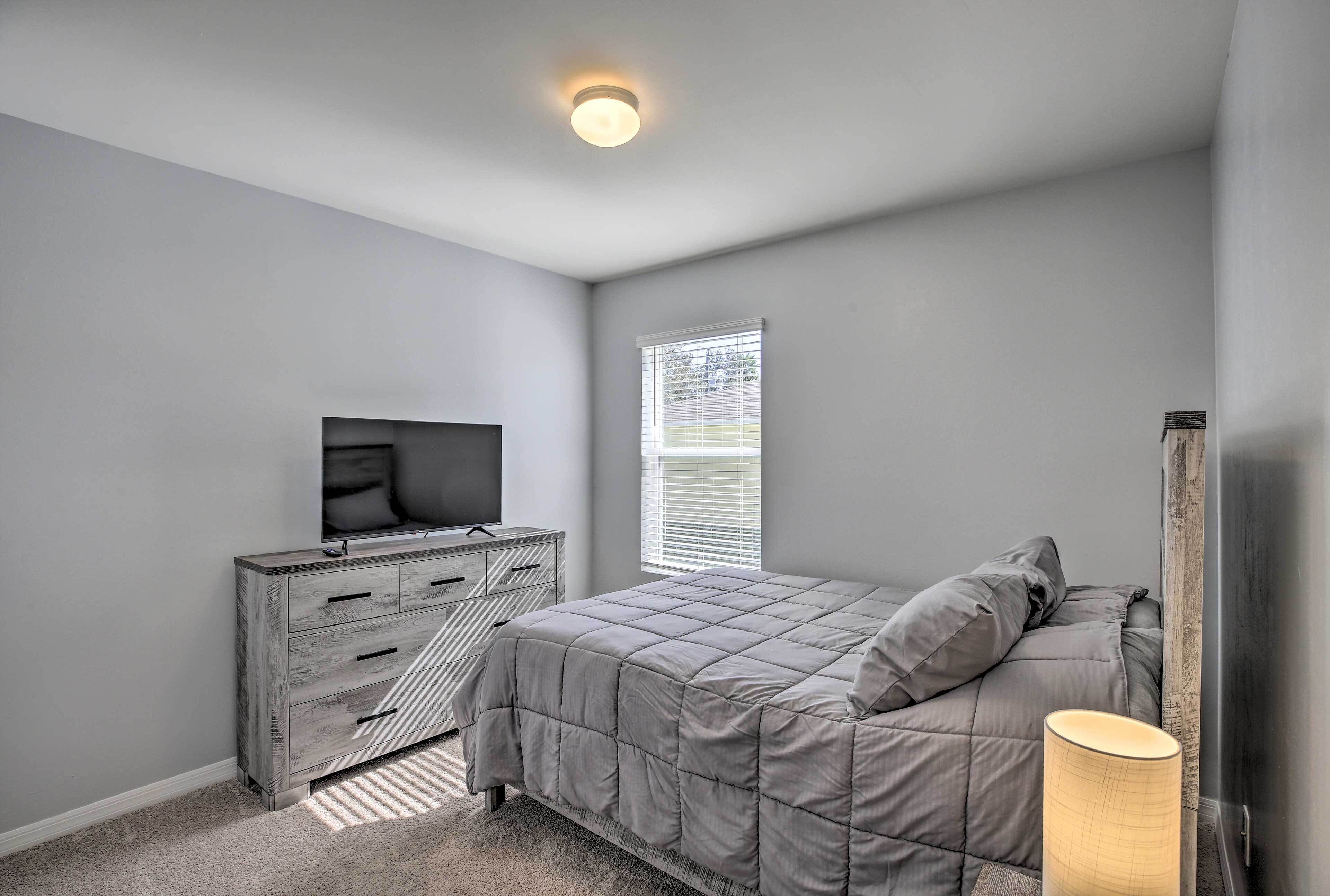 A bedroom with a bed, dresser, TV, window, and lamp.
