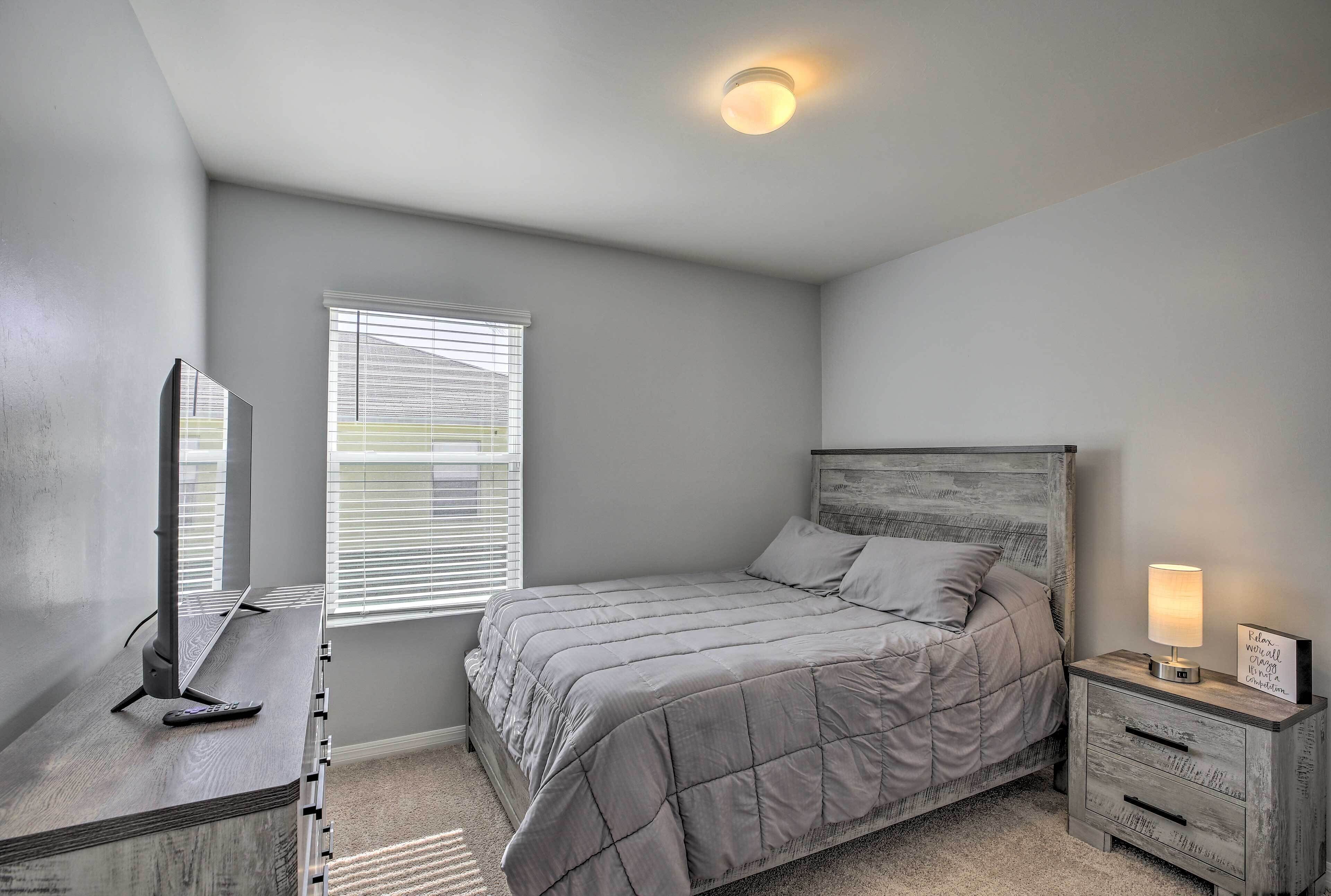 A bedroom with a bed, bedside table, lamp, and a window with blinds.