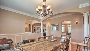 A spacious dining area with a wooden table and chairs, a chandelier, and a view into the kitchen.