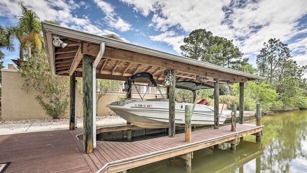 A wooden dock extending into a calm body of water with a covered boat storage area and a clear sky. - Luxury Palm Coast Home w/ Dock & Game Room! (Palm Coast)